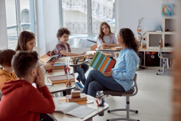 young-tutor-is-teaching-read-her-student-elementary-school-kids-sitting-desks-reading-books-classroom